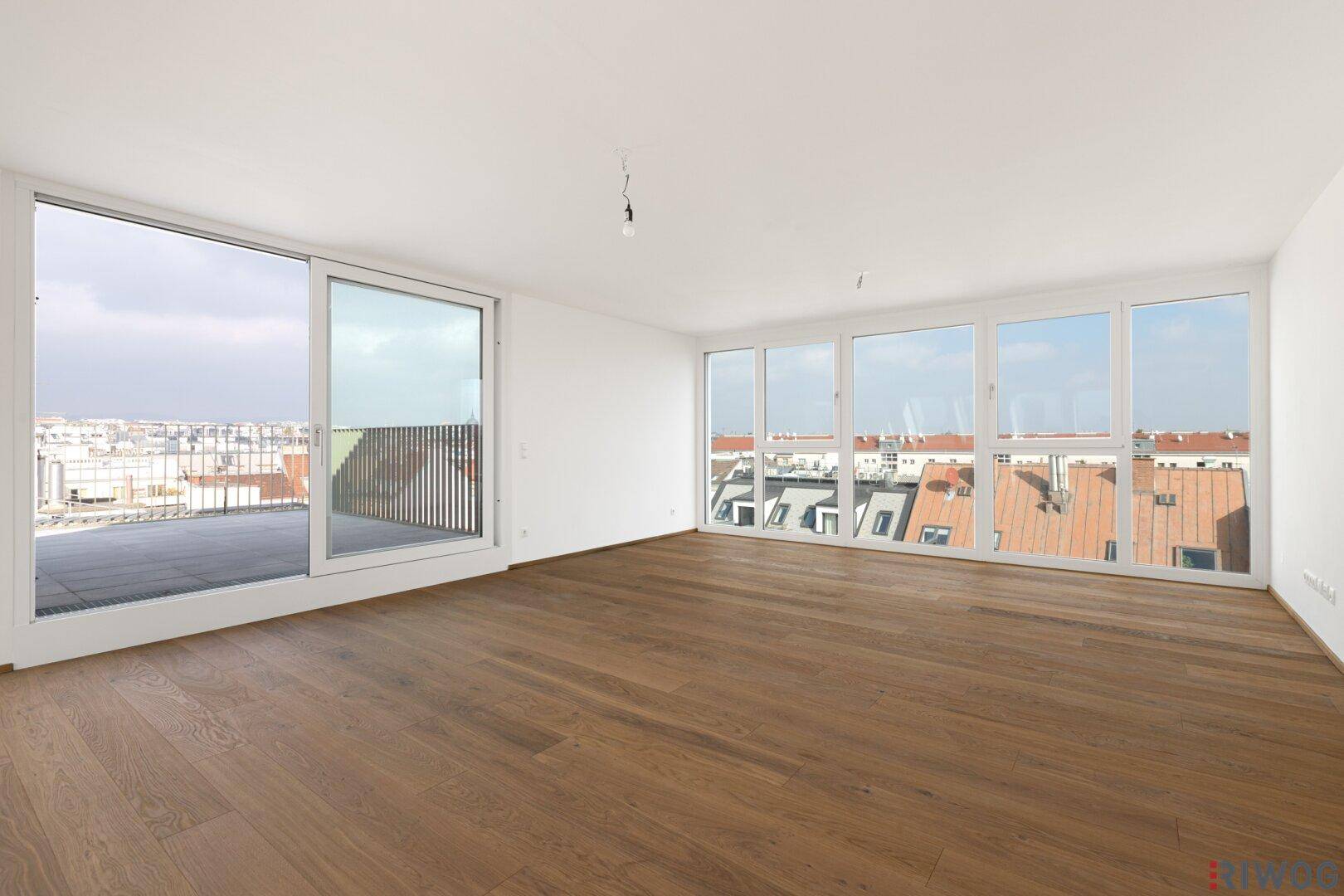 Heller, leerer Wohnraum mit großen Fenstern und Zugang zur Terrasse, bereit zur individuellen Gestaltung.