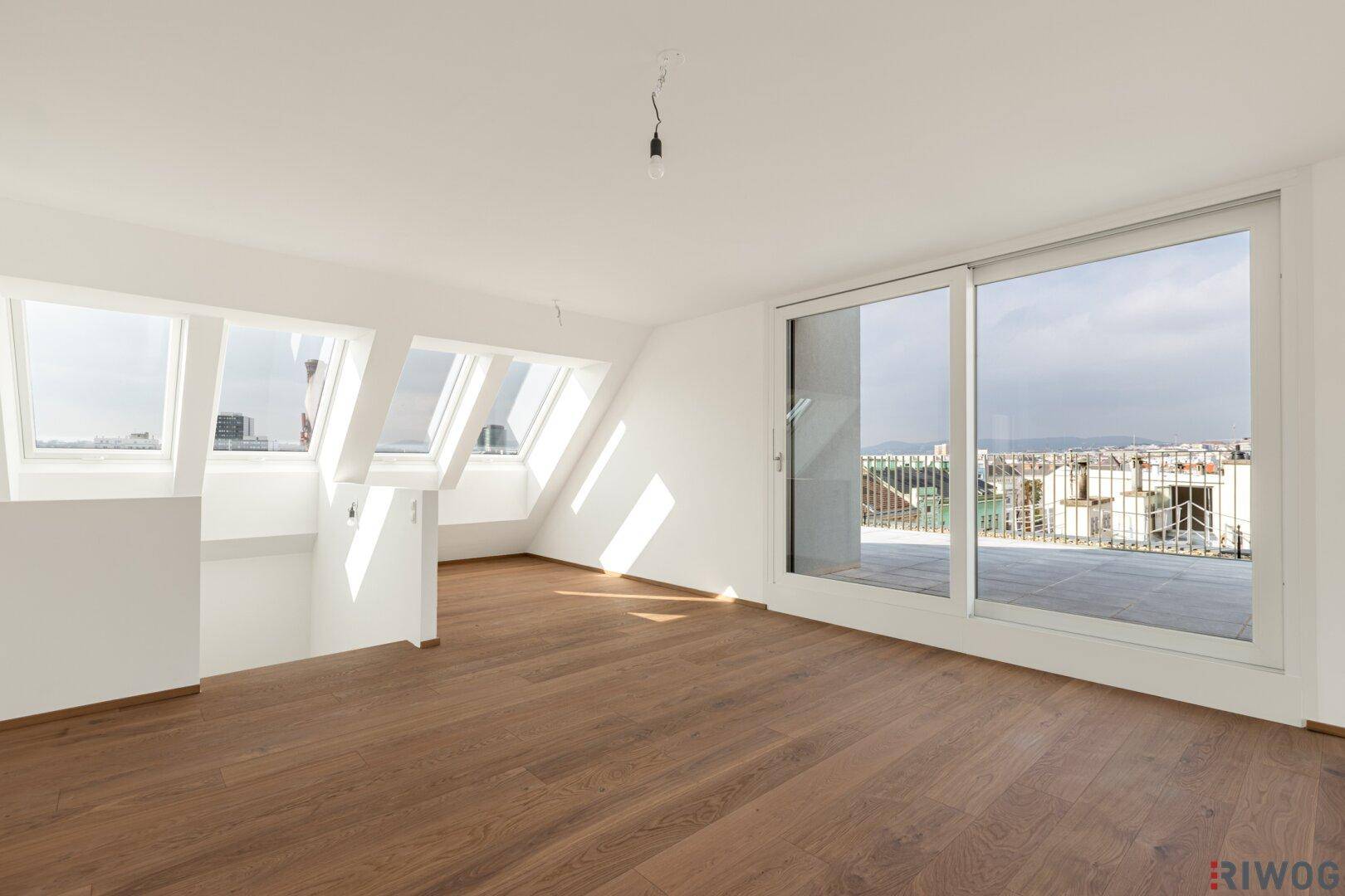 Lichtdurchfluteter Wohnraum im Dachgeschoss mit großen Fenstern und Zugang zur Terrasse.