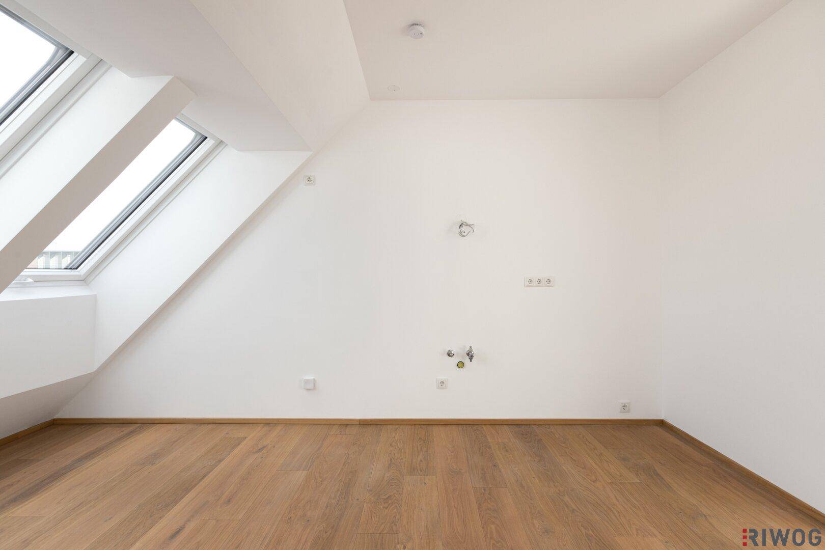 Kleiner Raum im Dachgeschoss mit Holzboden und Anschlüssen für eine mögliche Küchenzeile.