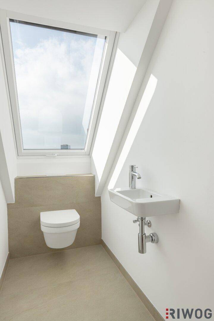 Modernes Gäste-WC im Dachgeschoss mit wandhängendem WC, kleinem Waschbecken und Dachfenster.