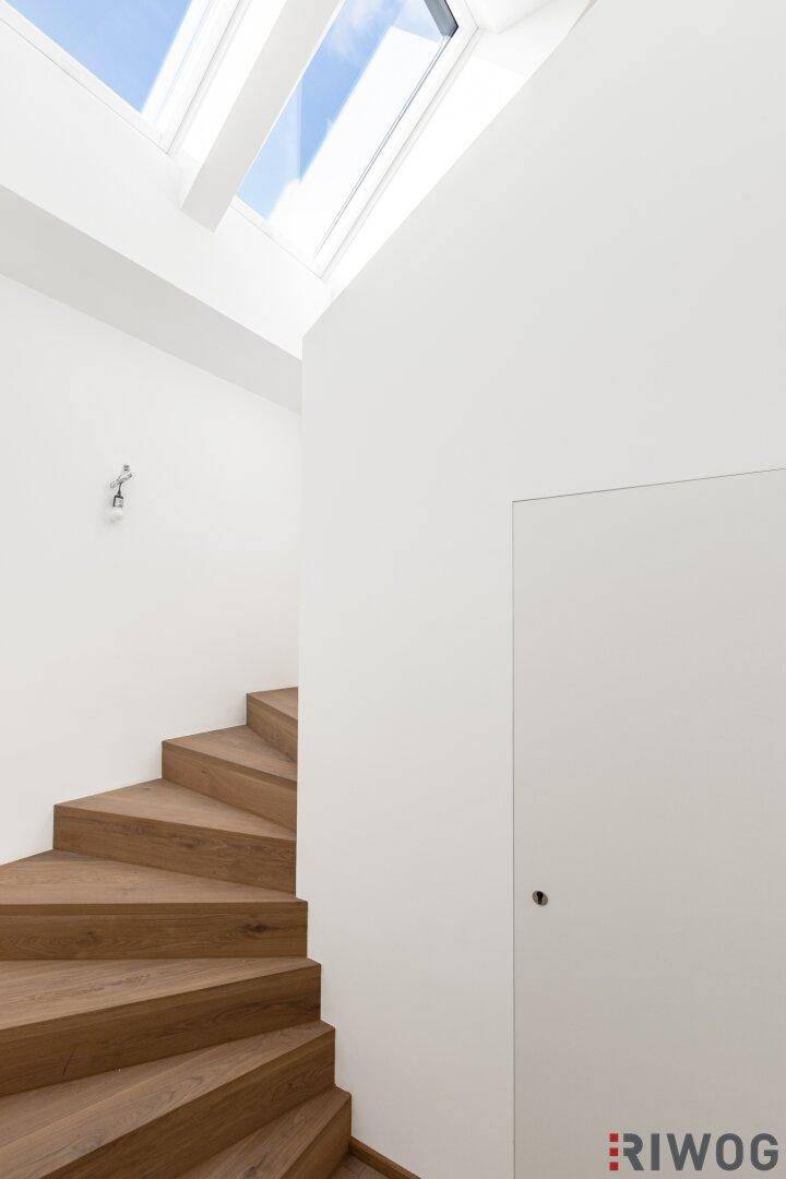Heller Treppenaufgang mit Holzstufen und Dachfenstern, die viel Tageslicht hereinlassen.