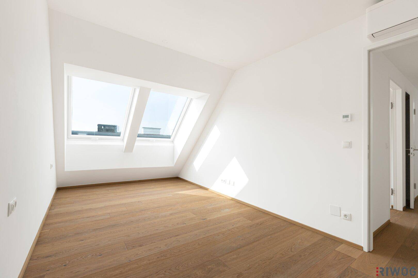 Geräumiges Schlafzimmer im Dachgeschoss mit Holzboden, Dachfenstern und Klimaanlage.
