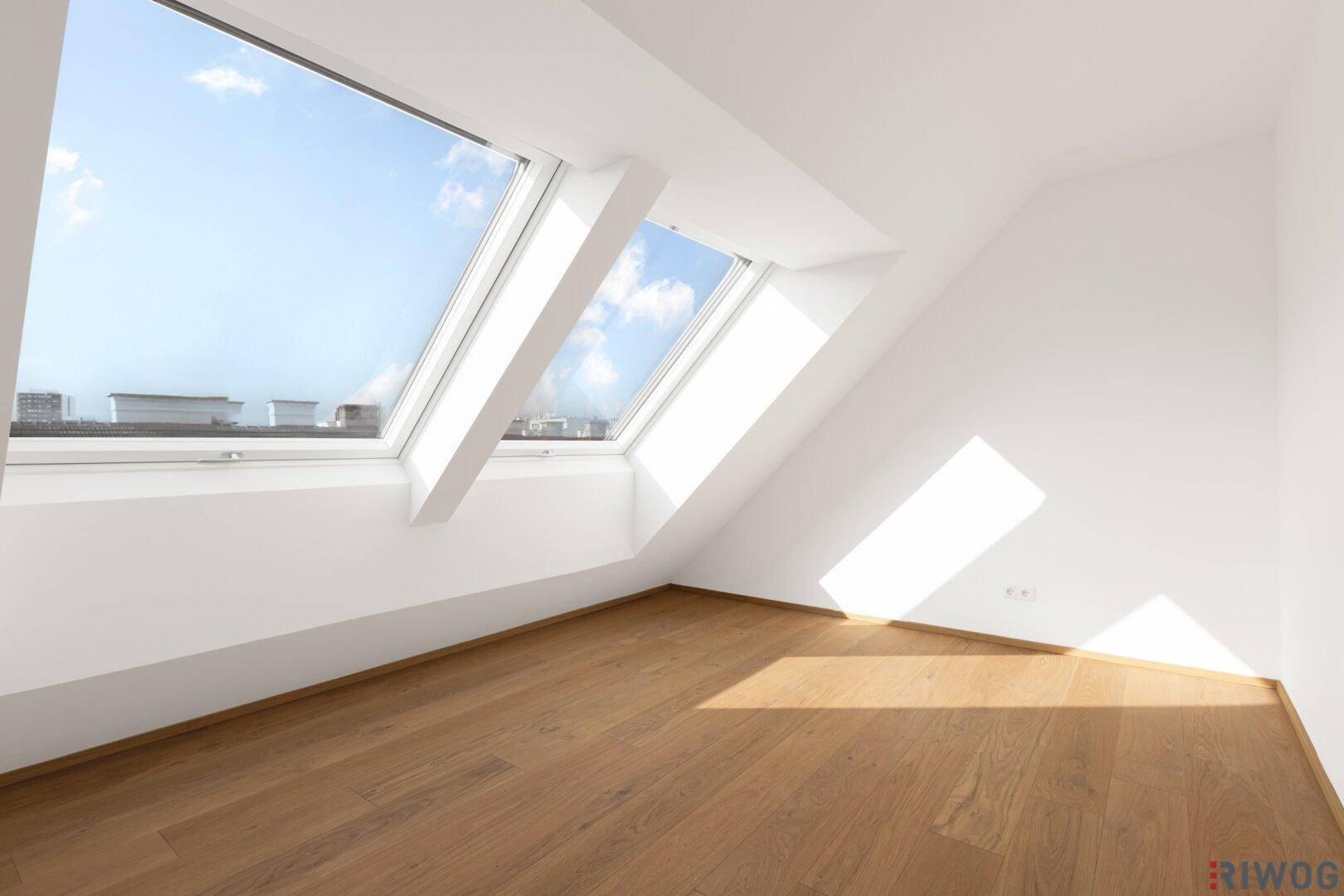 Helles Schlafzimmer im Dachgeschoss mit Holzboden und zwei großen Dachfenstern.