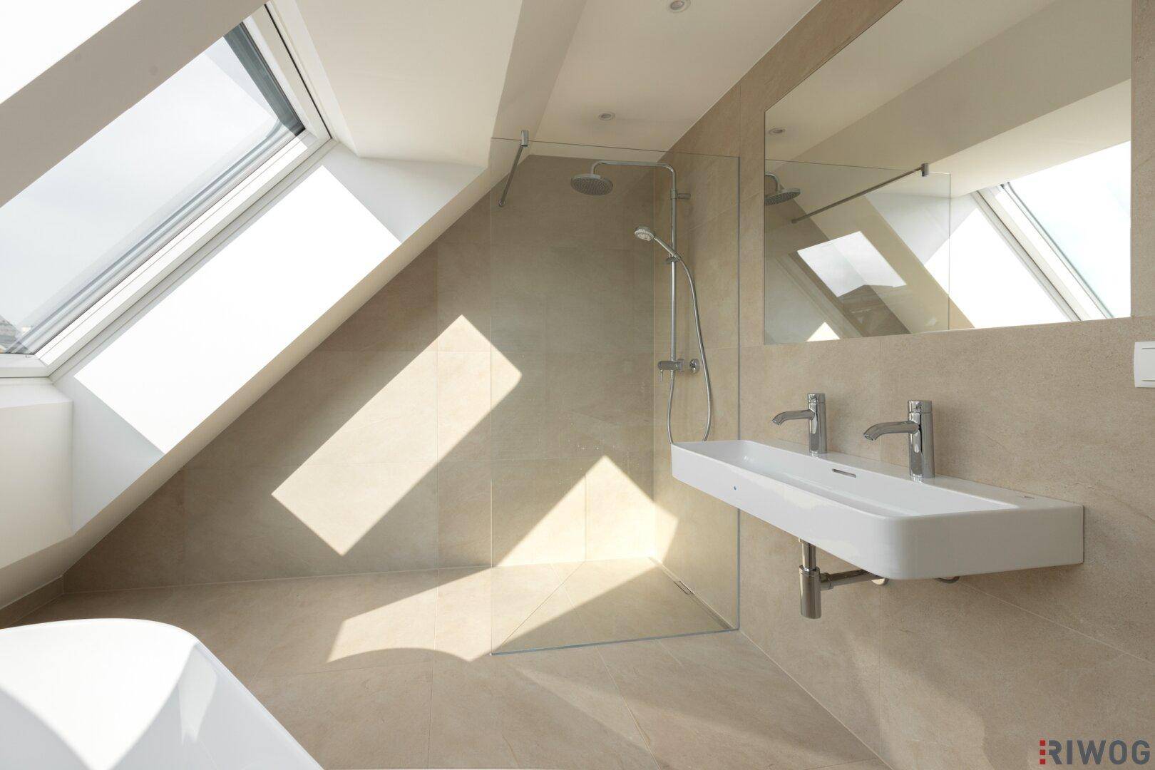 Modernes Badezimmer mit begehbarer Dusche, Doppelwaschbecken und viel Tageslicht durch Dachfenster.