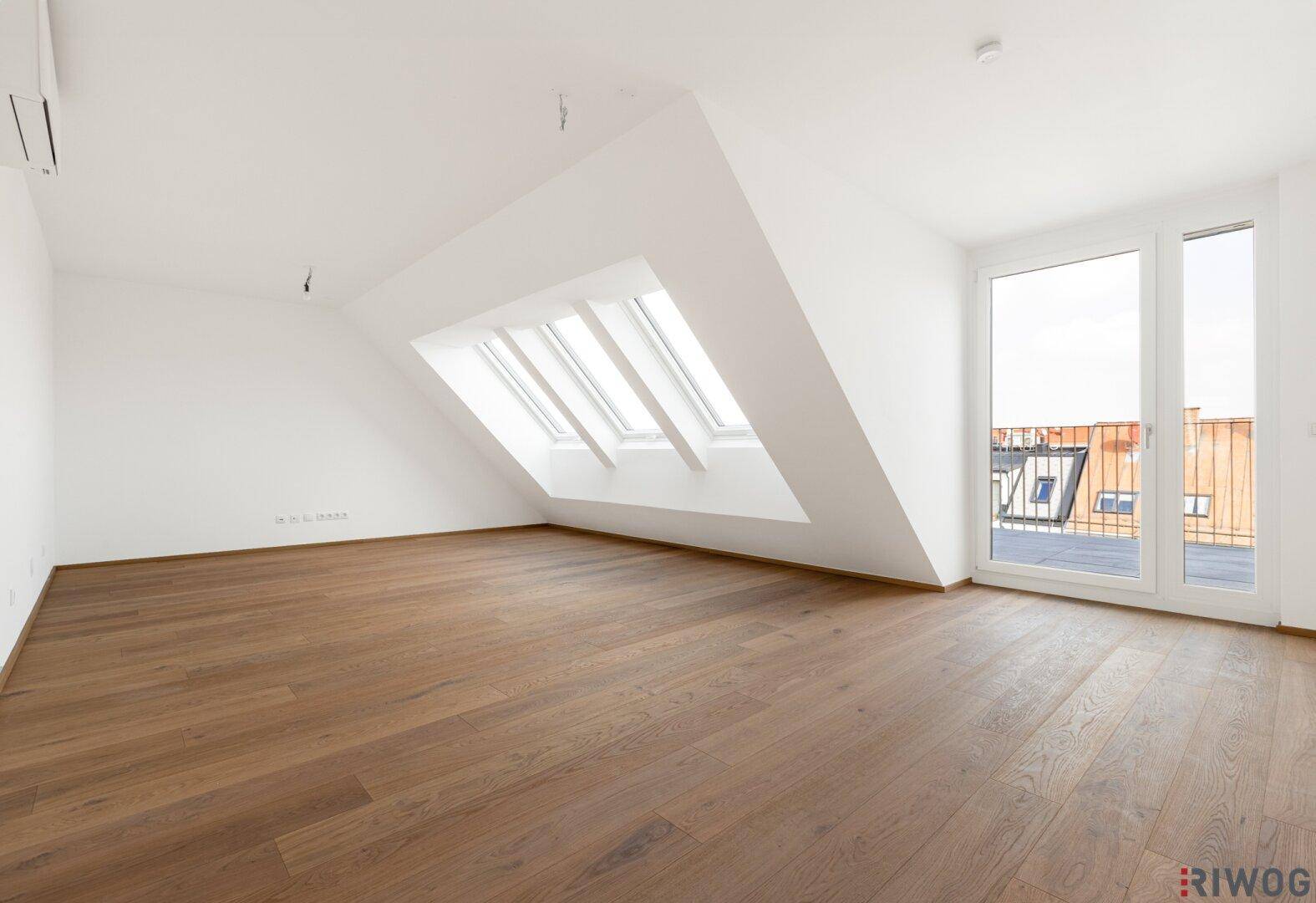 Heller Raum im Dachgeschoss mit Holzboden, Dachschrägen und Zugang zum Balkon.