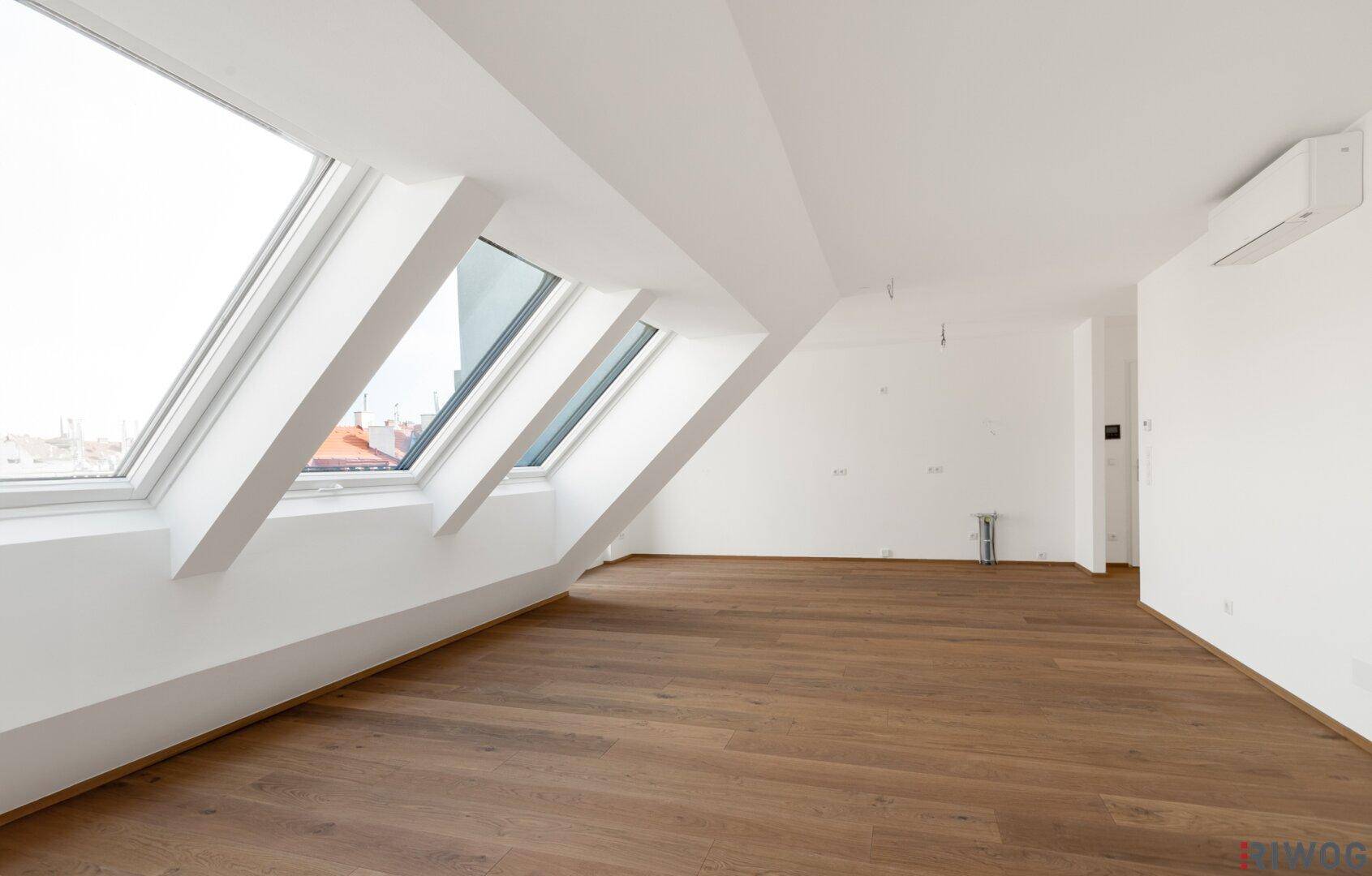 Lichtdurchfluteter Dachgeschossraum mit Holzboden, Dachschrägen und mehreren Dachfenstern.