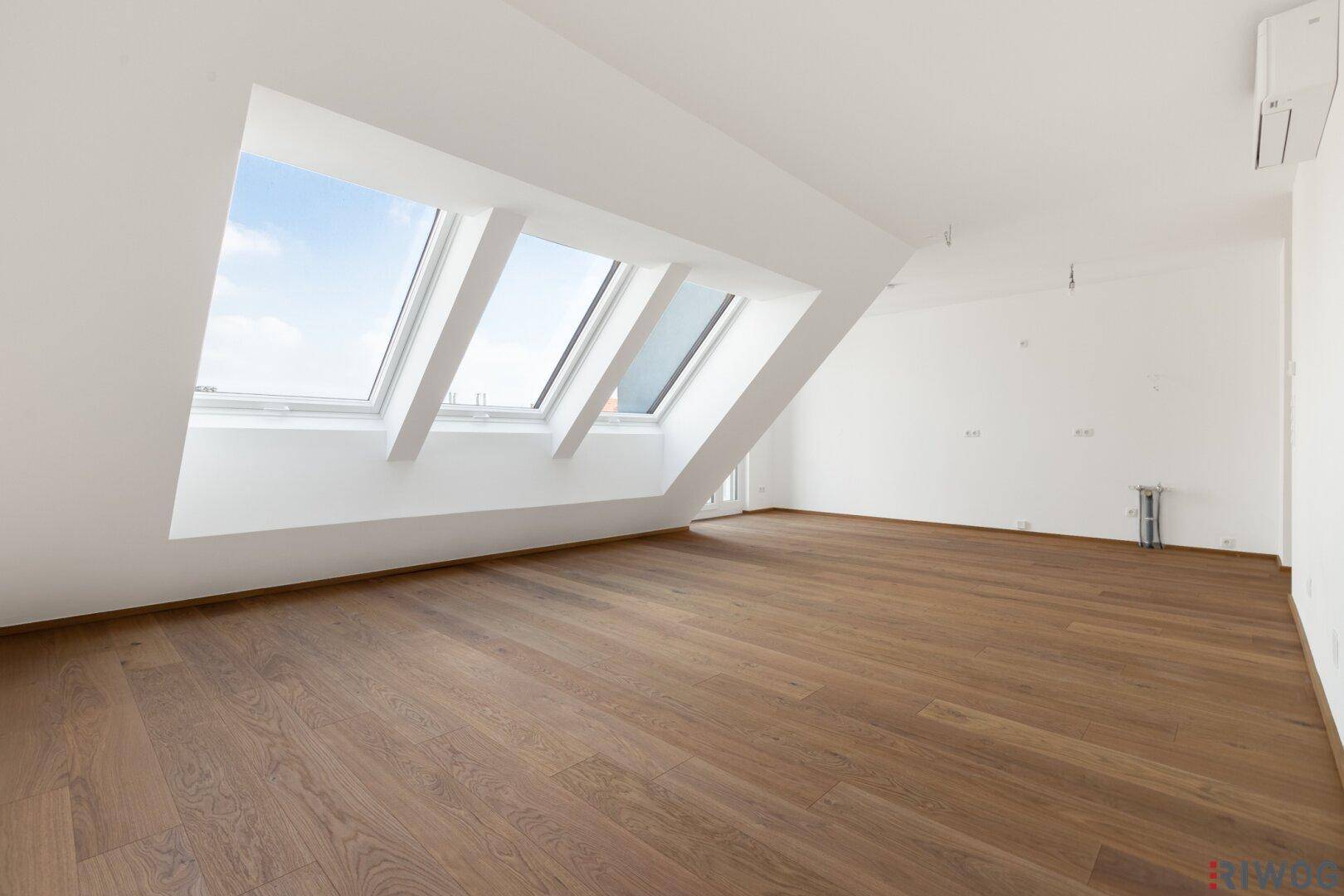 Geräumiger, heller Dachgeschossraum mit Holzboden, Dachschrägen und drei Dachfenstern.