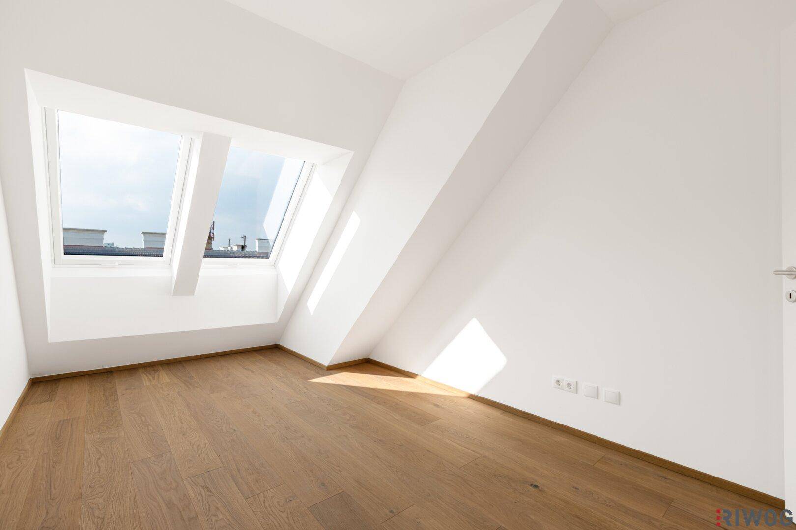 Lichtdurchfluteter Dachgeschossraum mit Holzboden, Dachschrägen und zwei großen Dachfenstern.