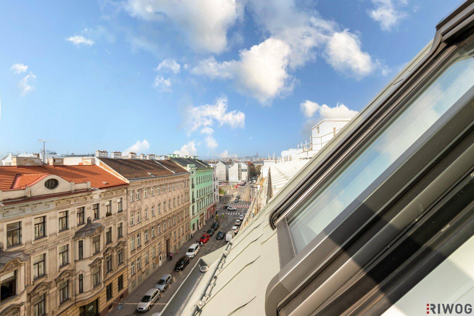 Blick aus einem Dachfenster auf eine belebte Stadtstraße und historische Gebäude.