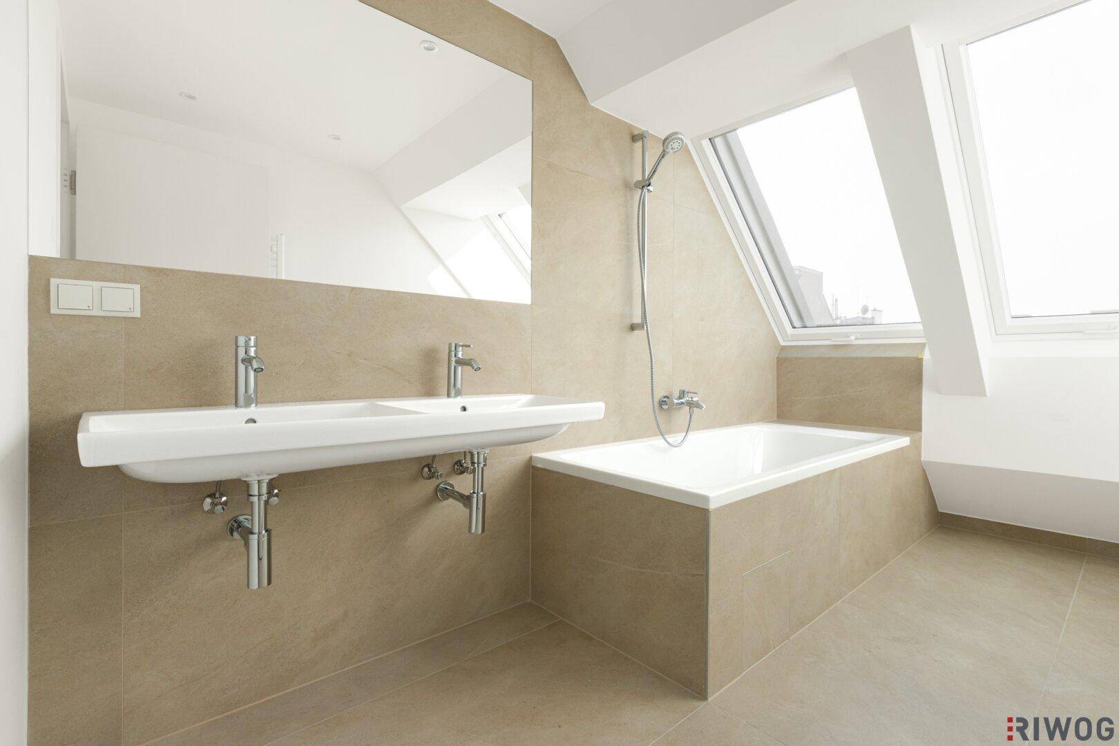 Modernes Badezimmer mit Doppelwaschbecken, Badewanne und Dachfenster unter der Schräge.