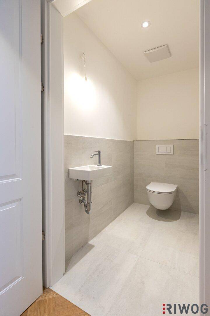 Modernes Gäste-WC mit Wand-WC, kleinem Waschbecken und hellen Fliesen.