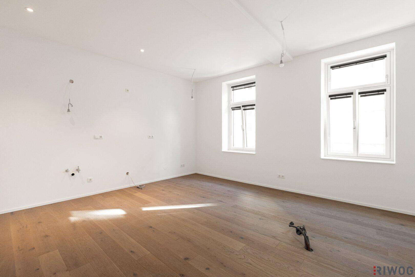 Geräumiger, heller Wohnraum mit Parkettboden und vorbereiteten Anschlüssen für Beleuchtung.