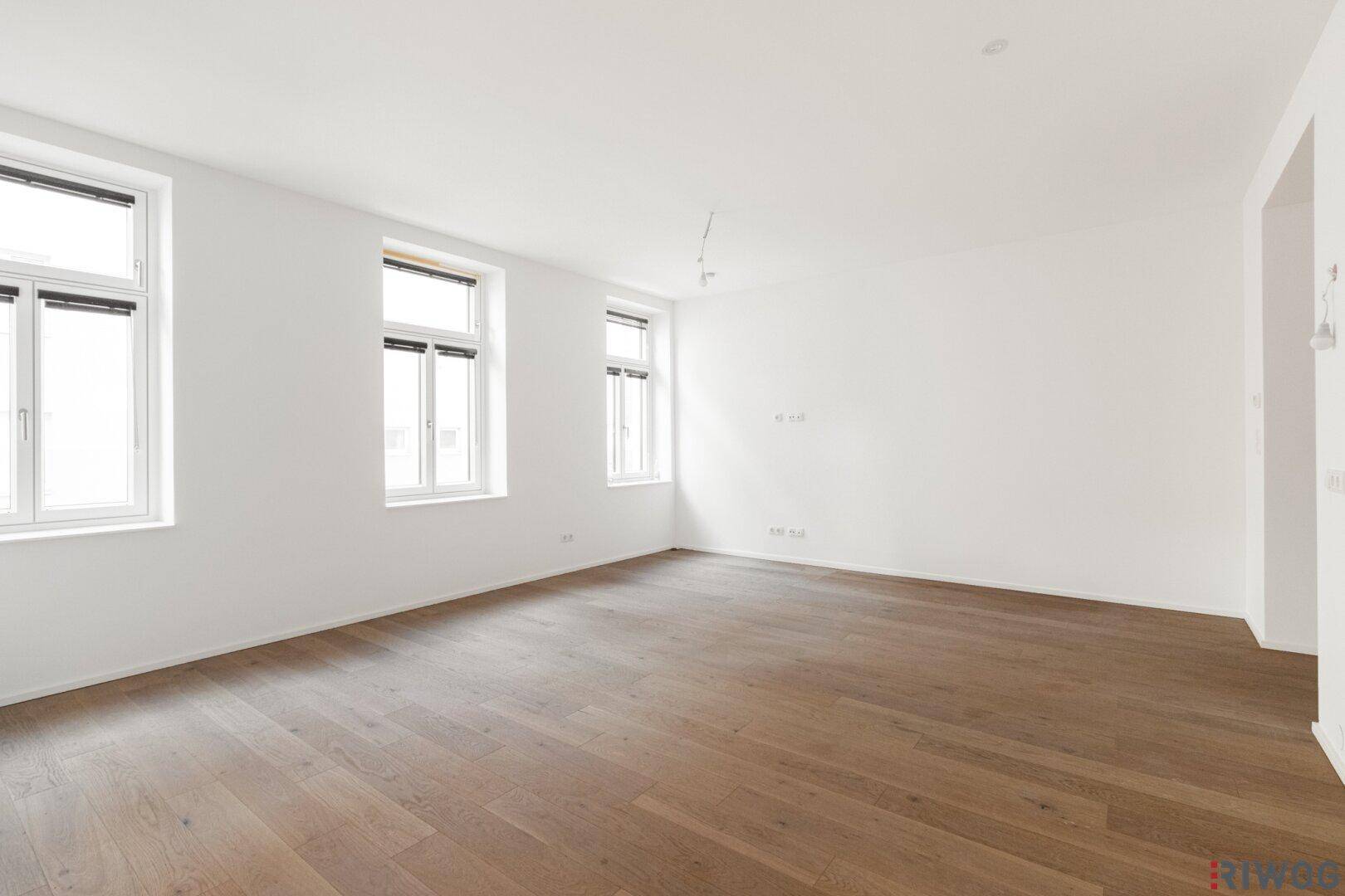 Lichtdurchfluteter Raum mit Holzboden und drei Fenstern, der vielseitig genutzt werden kann.