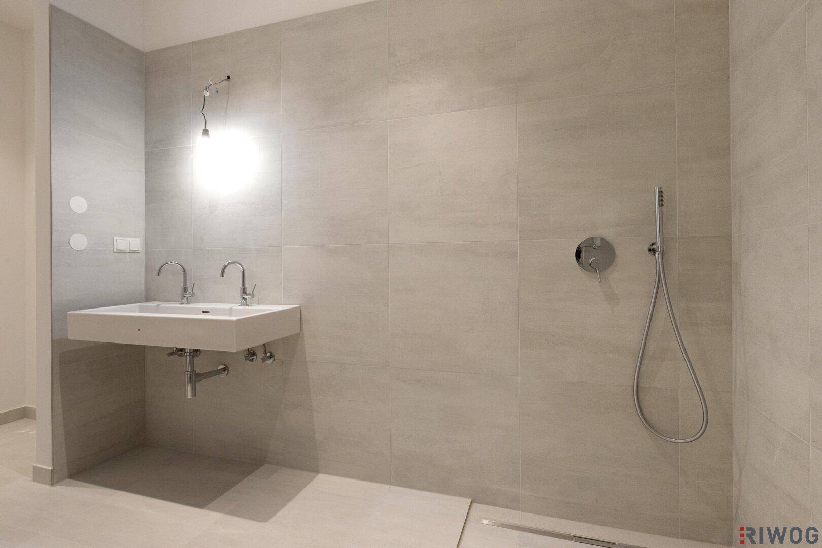 Modernes Badezimmer mit Doppelwaschbecken, großer begehbarer Dusche und hellgrauen Fliesen.