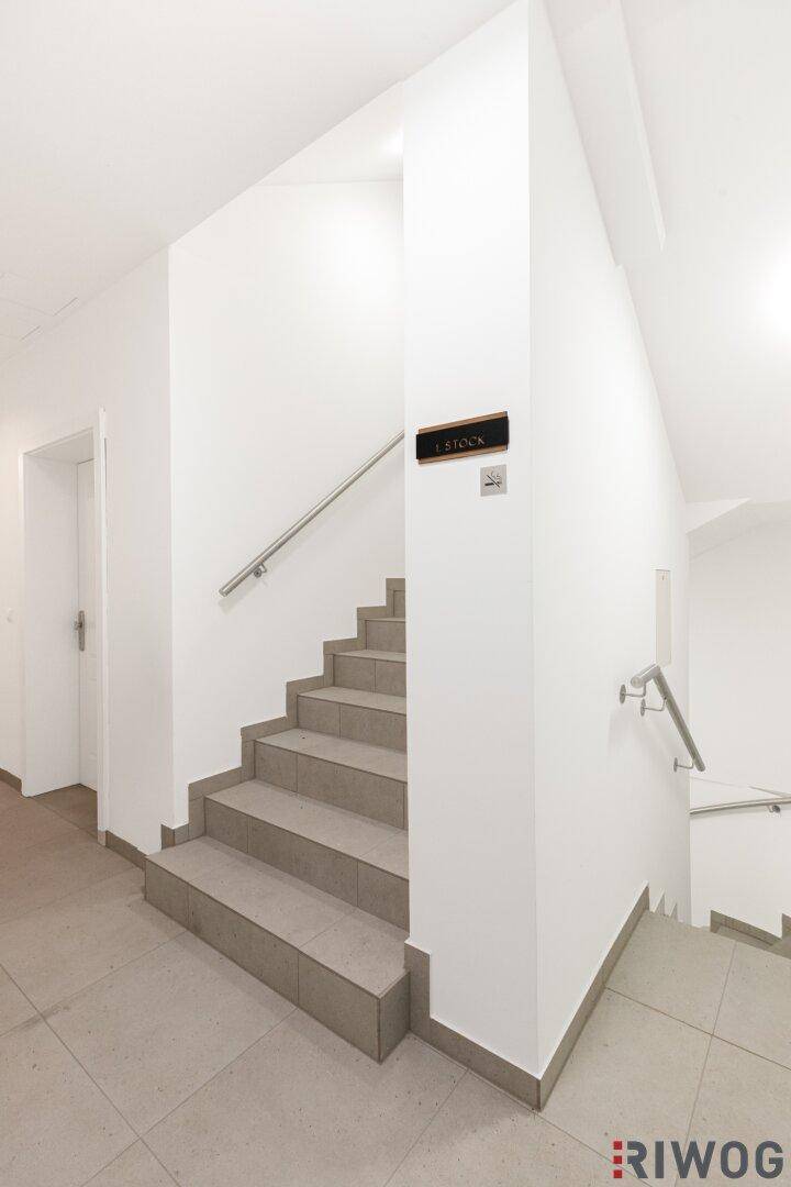 Helles Treppenhaus mit Fliesenboden, weißen Wänden und modernen Handläufen in einem gepflegten Gebäude.