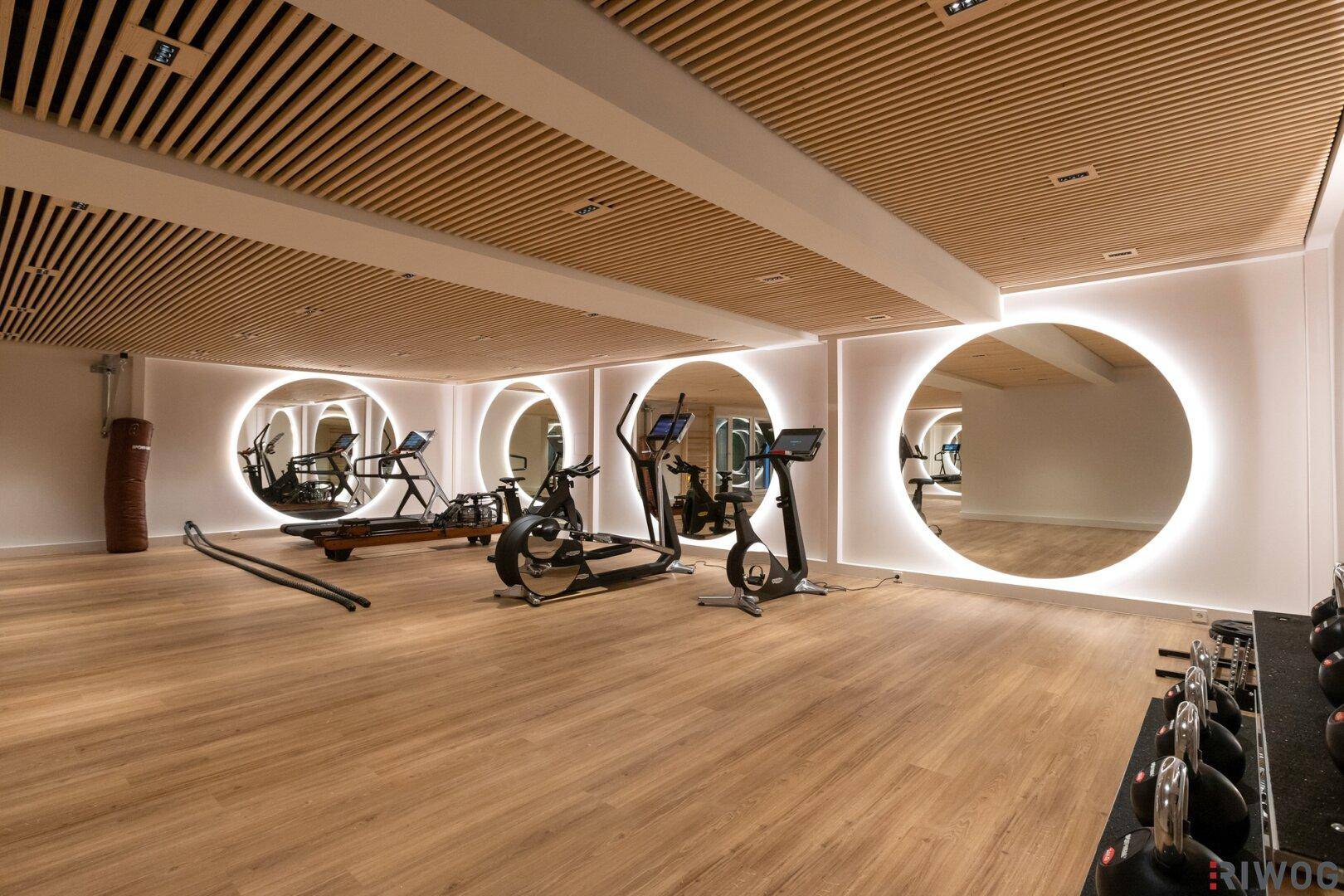 Gut ausgestatteter Fitnessraum mit modernen Trainingsgeräten und stilvoller Holzdeckenverkleidung.