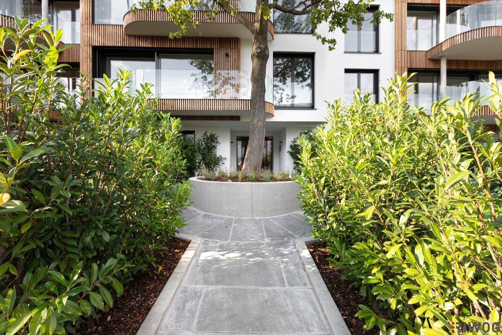 Moderne Wohnanlage mit Holzfassade, großen Fenstern und Balkonen, eingebettet in grüne Umgebung.