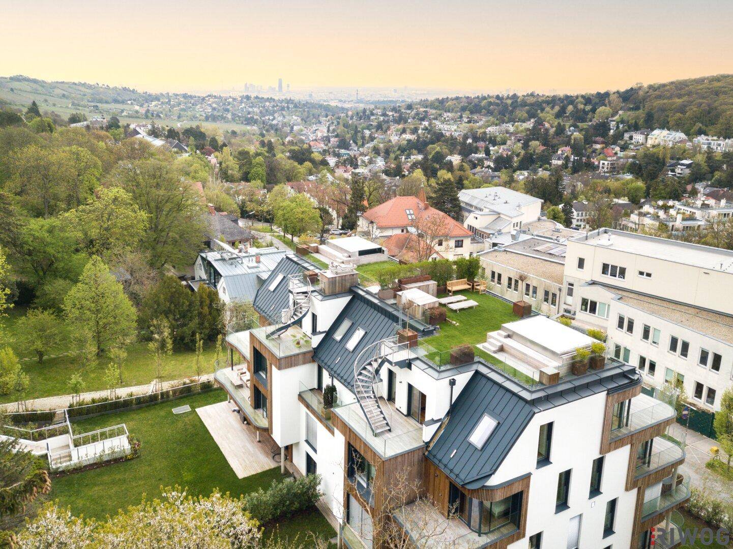 Weitläufige Luftaufnahme eines modernen Wohnkomplexes mit grünen Dächern und Stadtpanorama.