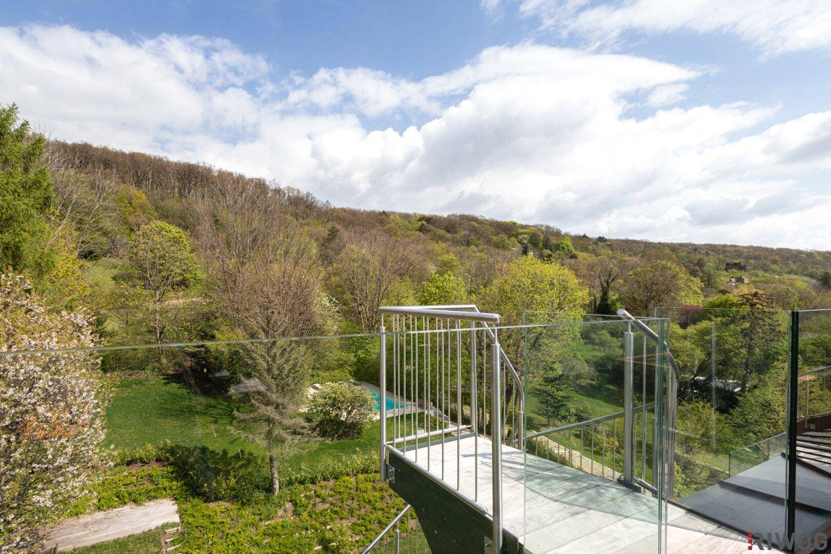 Dachterrasse mit Rasenfläche und Holzpodest, umgeben von grünen Hügeln unter klarem Himmel.