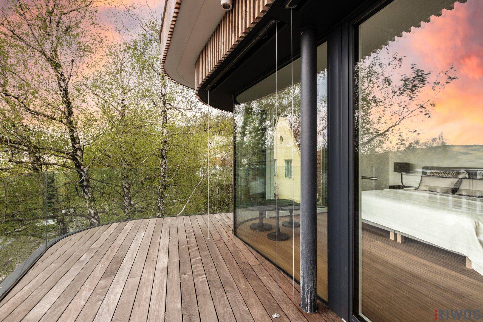 Geräumige Holzterrasse mit gebogener Glasfront und Blick auf die grüne Umgebung.