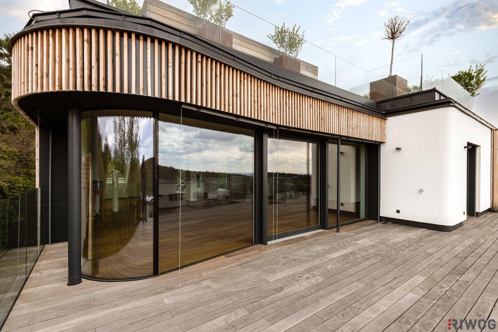 Stilvolle Holzterrasse mit gebogener Glasfront und Holzverkleidung, integriert in moderne Architektur.