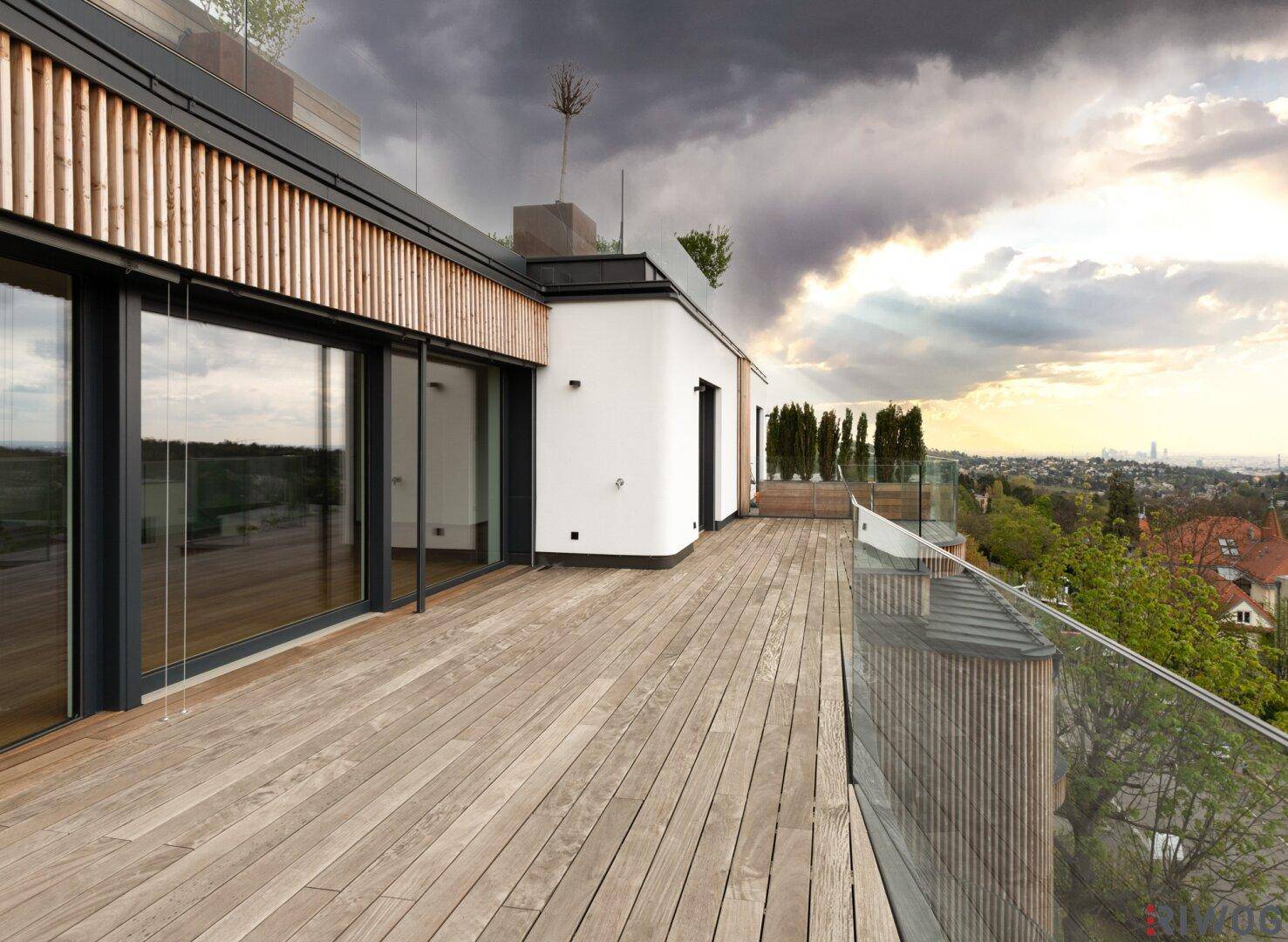 Große Holzterrasse mit Glasgeländer und weitem Blick über die Stadt und die umliegende Landschaft.