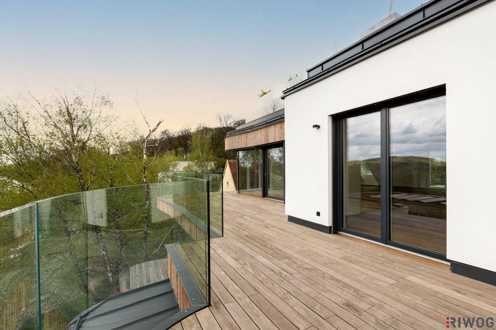 Geräumige Holzterrasse mit Glasgeländer und Blick ins Grüne, perfekt für entspannte Stunden im Freien.