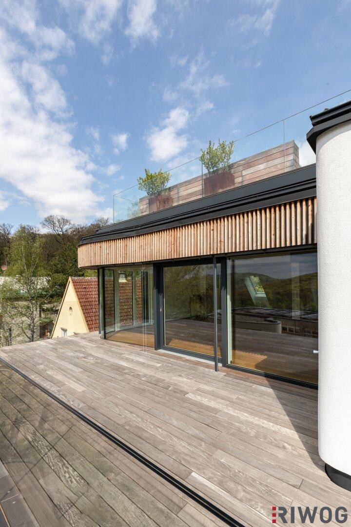 Moderne Holzterrasse mit Glasbrüstung und Holzverkleidung, umgeben von üppigem Grün.