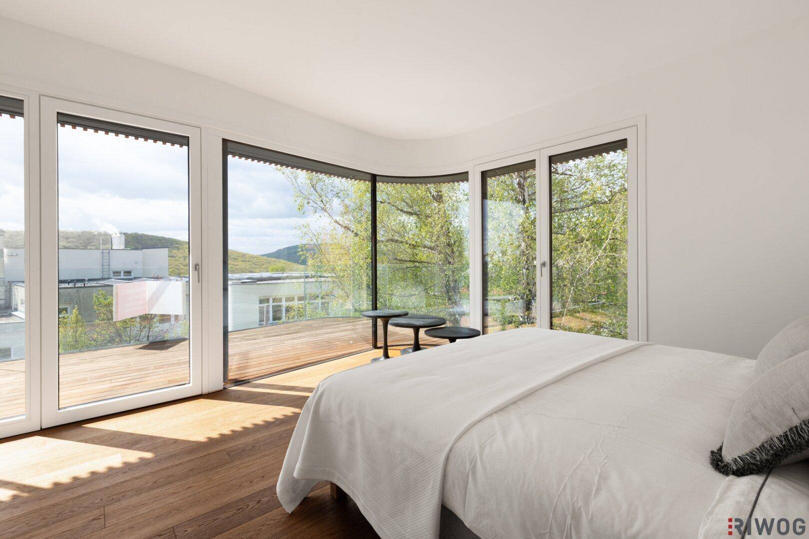 Modernes Schlafzimmer mit gebogener Glasfront und Holzboden, umgeben von üppiger Natur.
