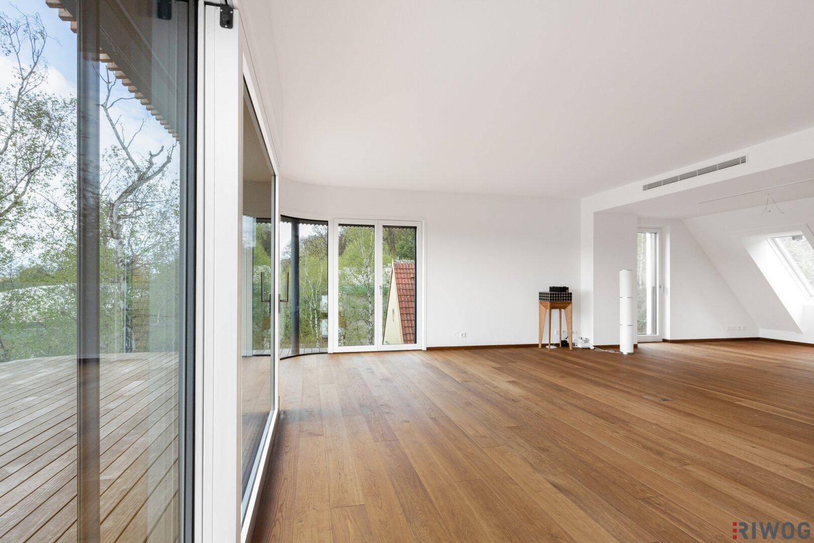 Lichtdurchfluteter Wohnbereich mit breiten Fensterfronten und hochwertigem Holzboden, ideal für offenes Wohnen.