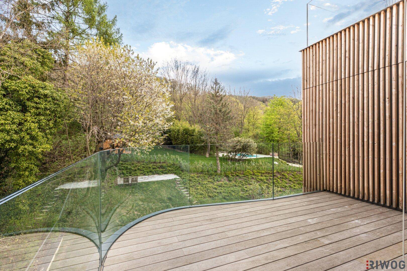 Moderne Holzterrasse mit gebogener Glasfront und Holzverkleidung, bietet Zugang zu einem Innenraum.