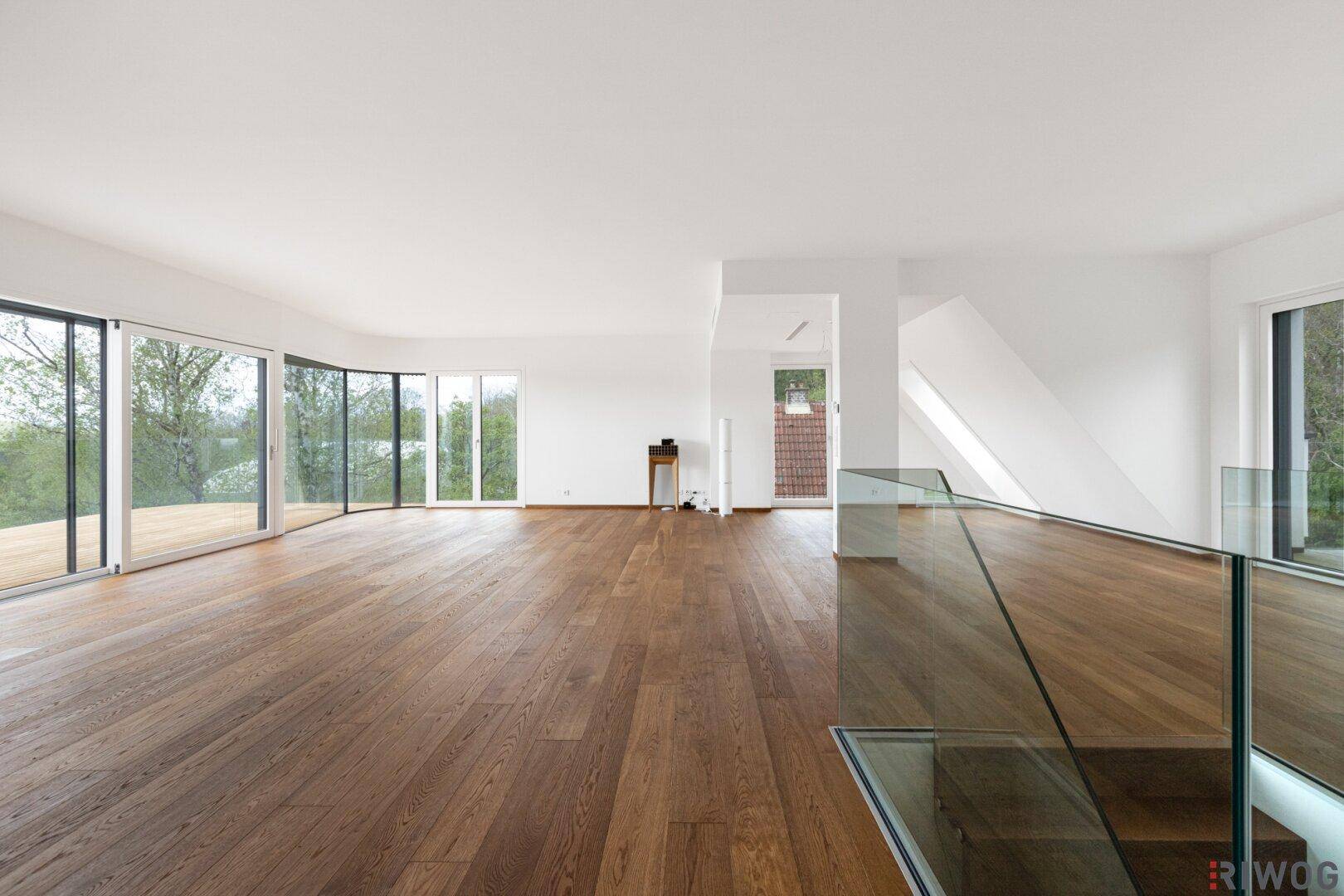 Großzügiger Wohnraum mit Holzboden und moderner Glasbrüstung, die den Blick auf die Umgebung freigibt.