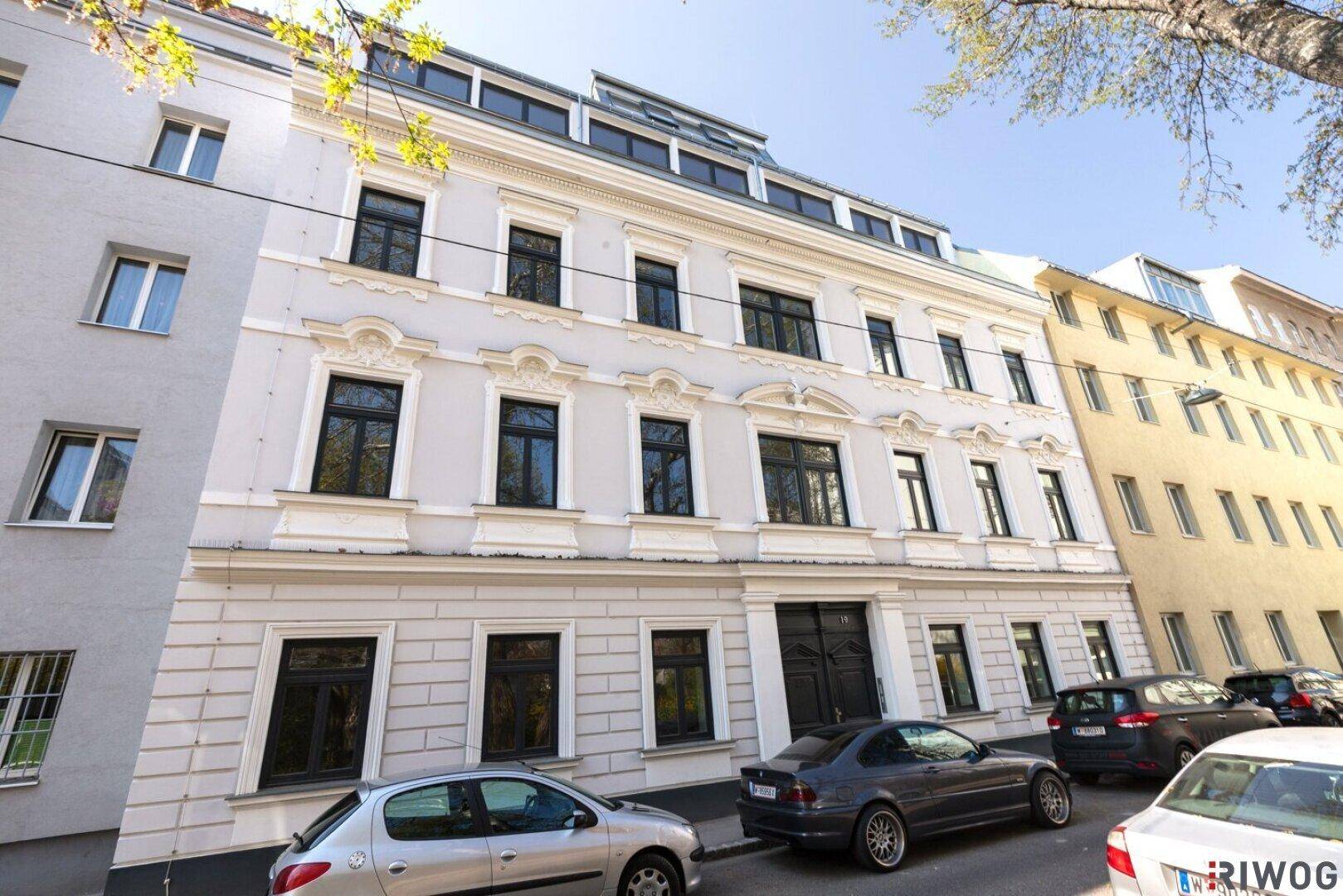 Historisches Mehrfamilienhaus mit klassischer Fassade und geparkten Autos auf der Straße davor.