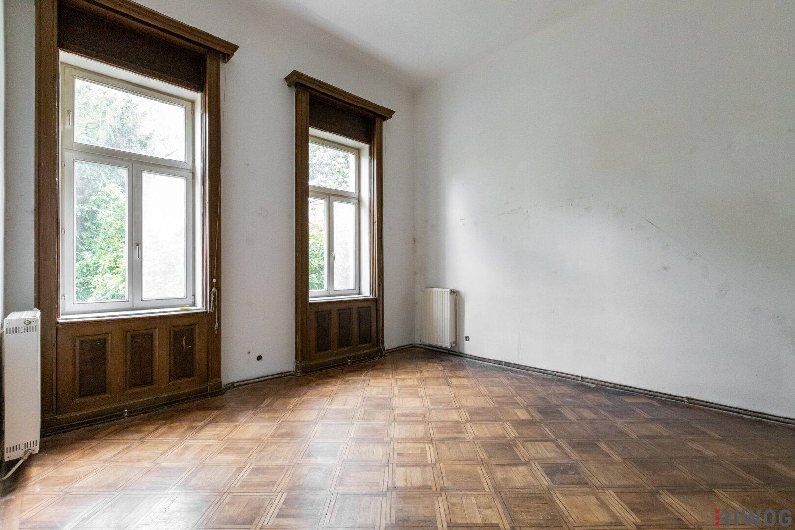 Heller Raum mit klassischem Parkettboden und hohen Fenstern, die viel Tageslicht hereinlassen.