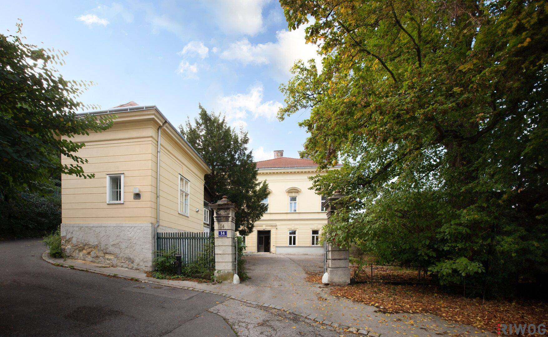 Der elegante Eingangsbereich der Villa von der Straße aus, umgeben von altem Baumbestand.