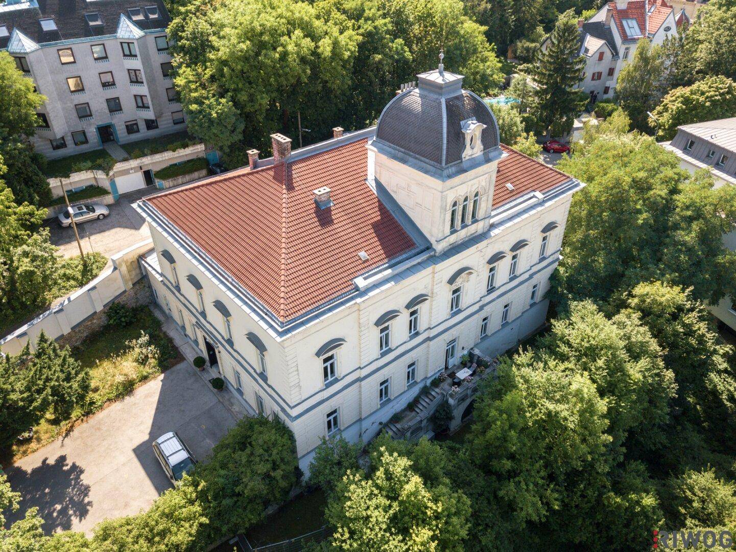 Historisches Gebäude von oben mit rotem Dach und umgebender dichter Vegetation.