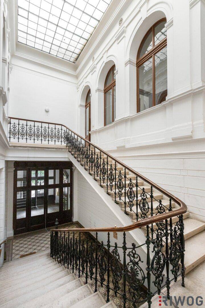 Eindrucksvolles Treppenhaus mit schmiedeeisernem Geländer, hohen Decken und Oberlicht.
