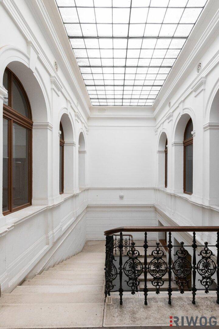 Helles Treppenhaus mit elegantem Geländer und großem Glasdach für viel Tageslicht.
