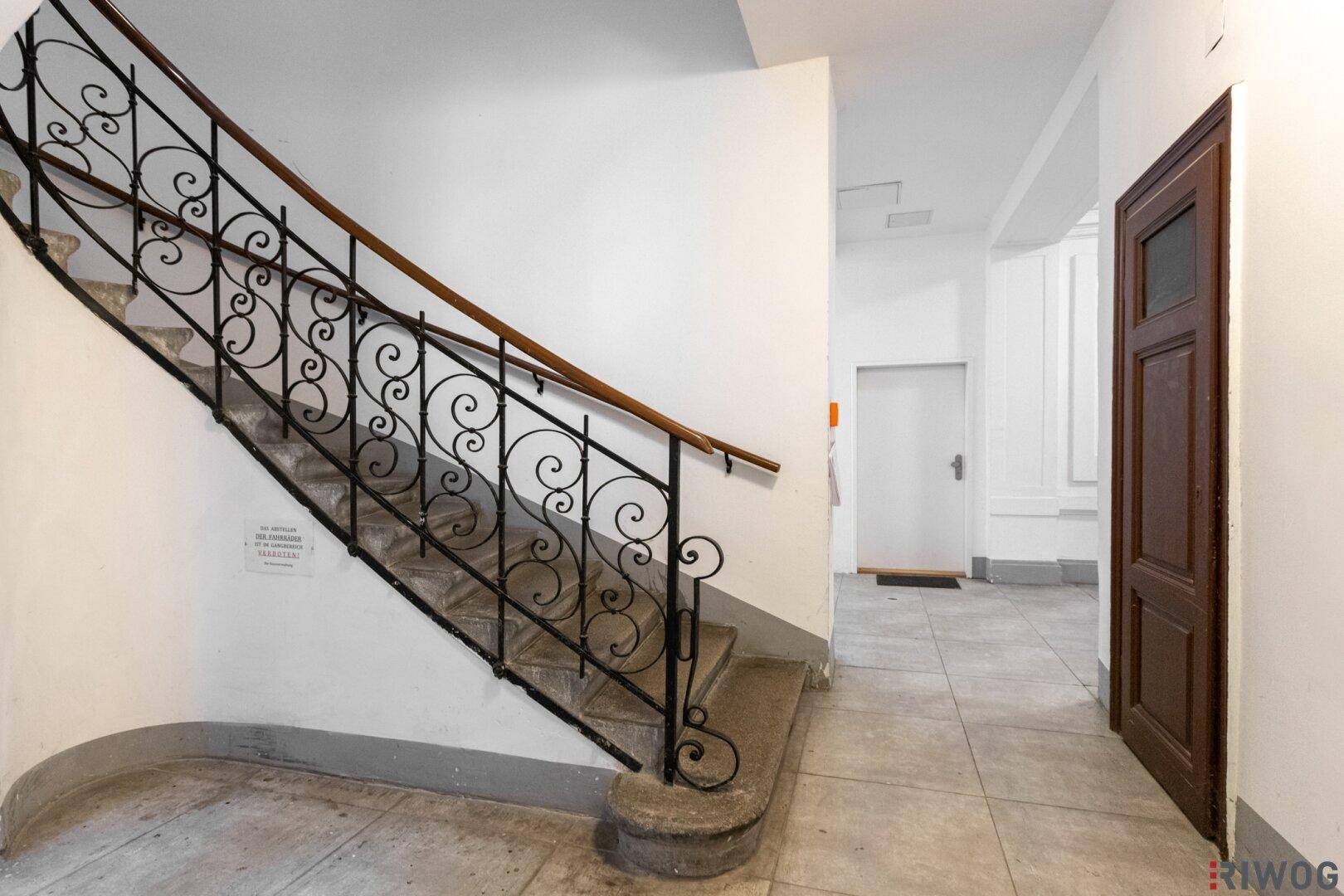 Historisches Treppenhaus mit schmiedeeisernem Geländer und Steinstufen in einem Altbau.