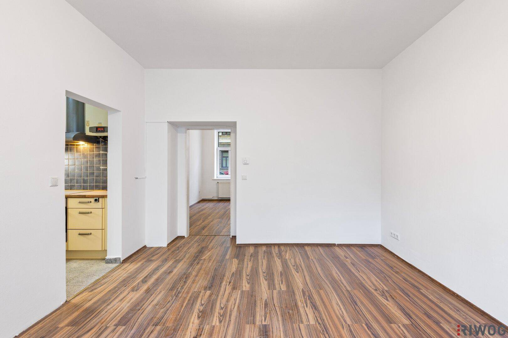 Heller Wohnbereich mit Holzboden und offenem Zugang zur Küche und einem weiteren Zimmer.