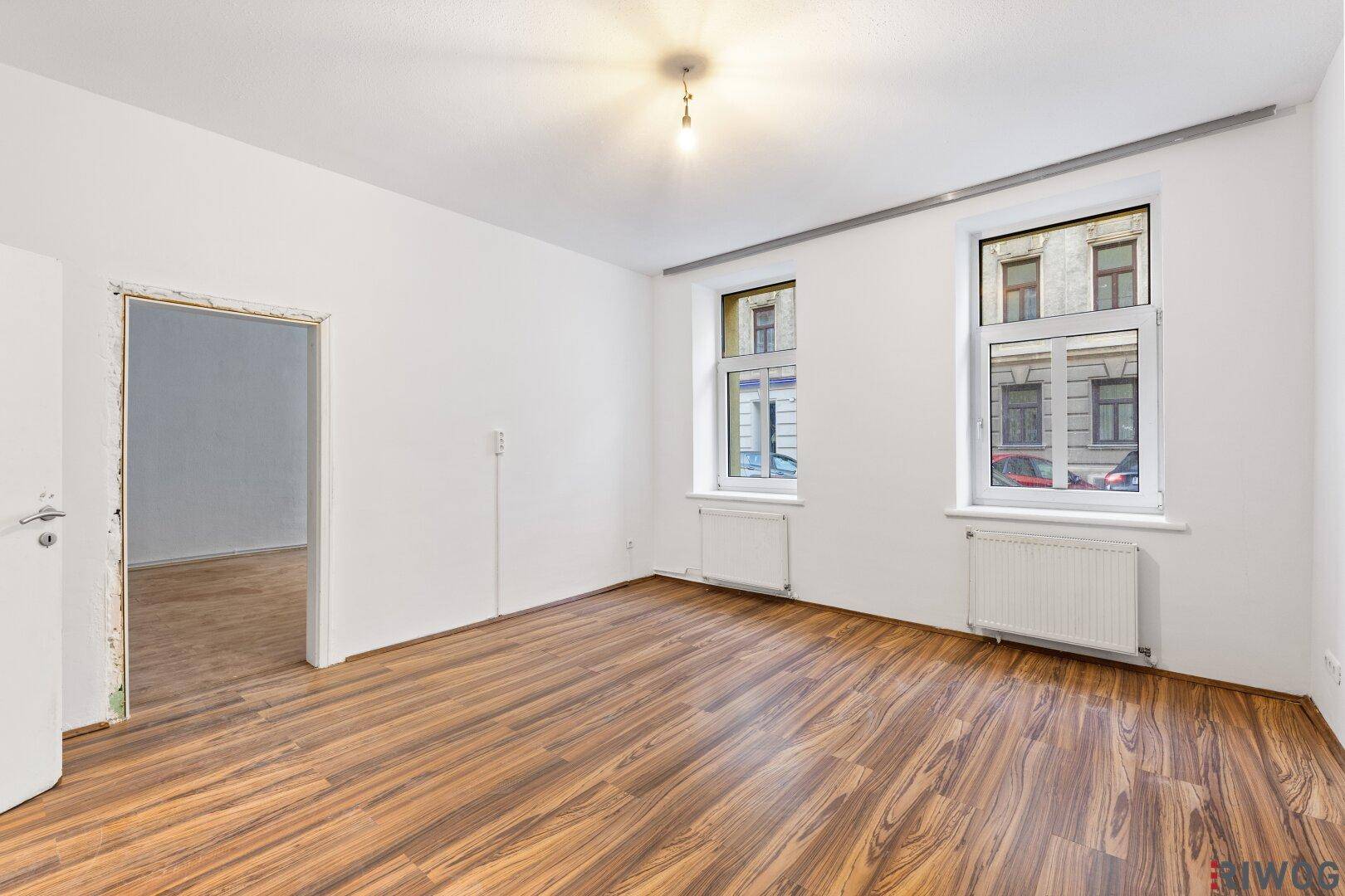 Geräumiges Wohnzimmer mit Holzboden und Blick auf die Stadt durch große Fenster.