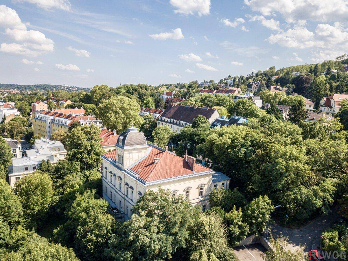 Luftaufnahme des historischen Gebäudes mit rotem Ziegeldach und umgebenden Bäumen.