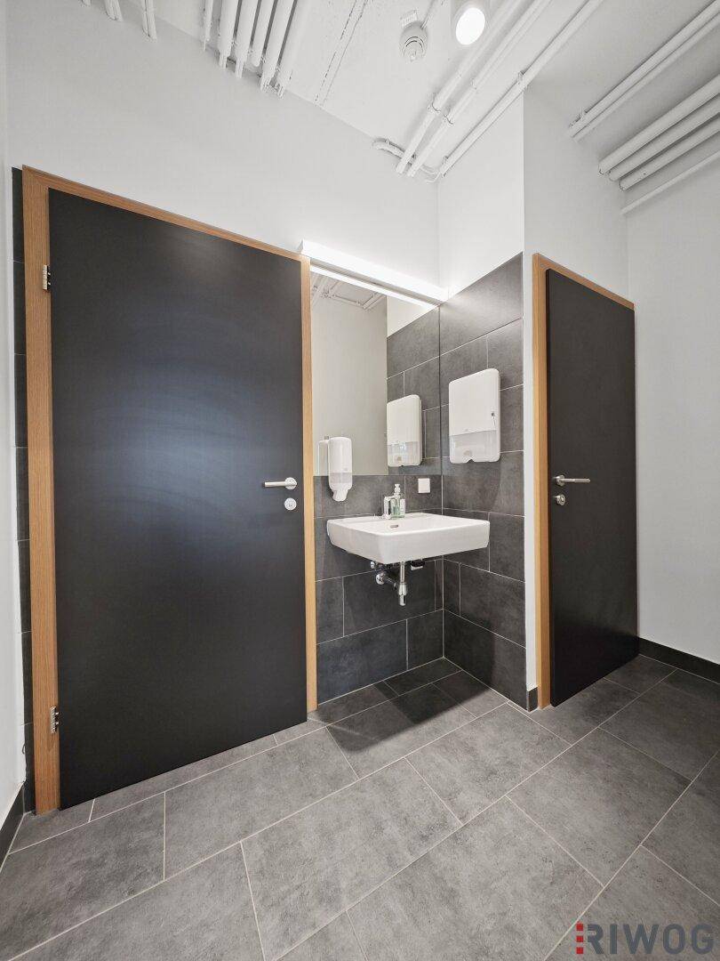 Modernes Badezimmer mit dunklen Fliesen, einem schwebenden Waschbecken und zwei schwarzen Türen mit Holzrahmen.