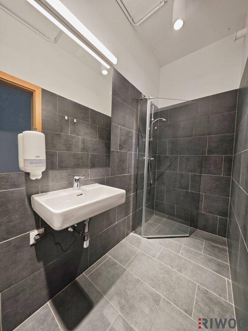 Modernes Badezimmer mit dunklen Fliesen, einer Glasdusche und einem schwebenden Waschbecken, sehr stilvoll.