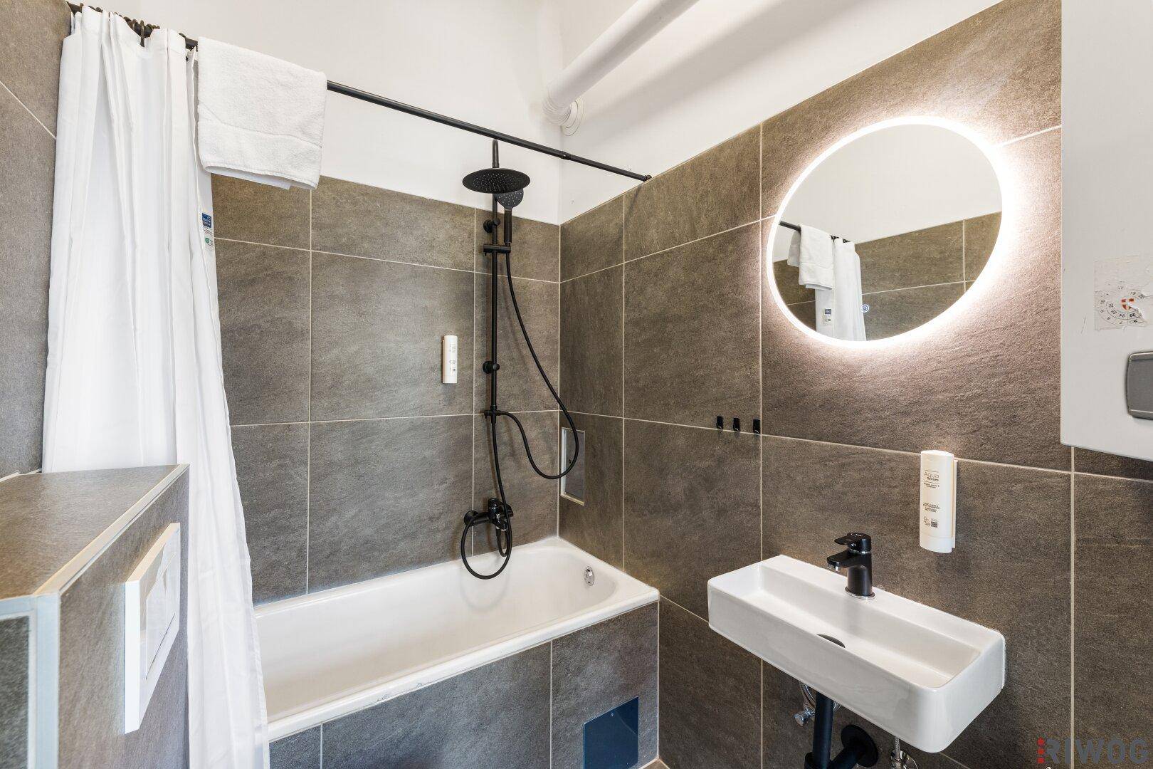 Modernes Badezimmer mit Badewanne, Dusche und beleuchtetem Spiegel.
