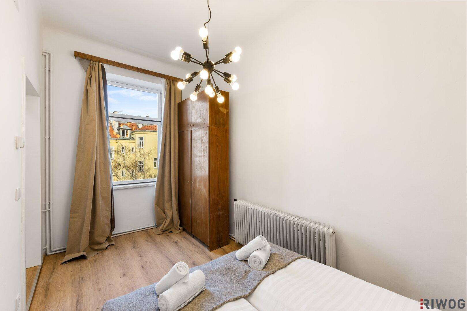 Helles Schlafzimmer mit Einzelbett, Holzschrank und Fensterblick.