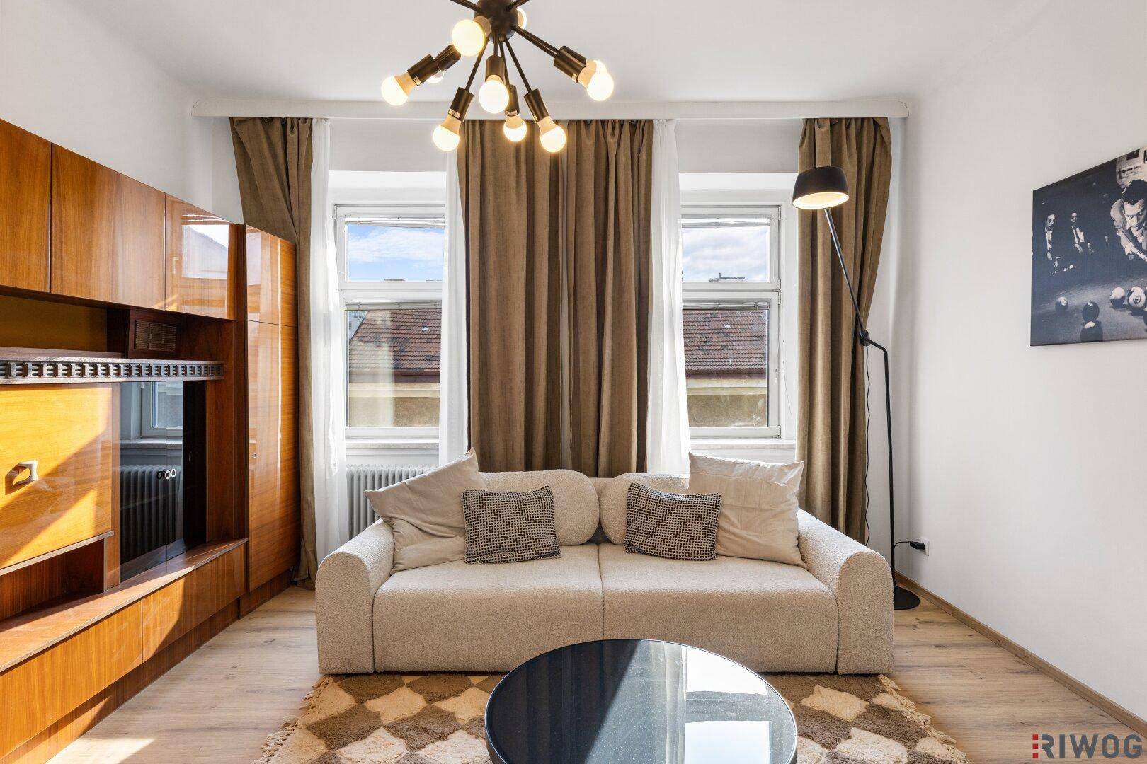 Gemütlicher Wohnbereich mit beiger Couch, großen Fenstern und stilvoller Deckenleuchte.