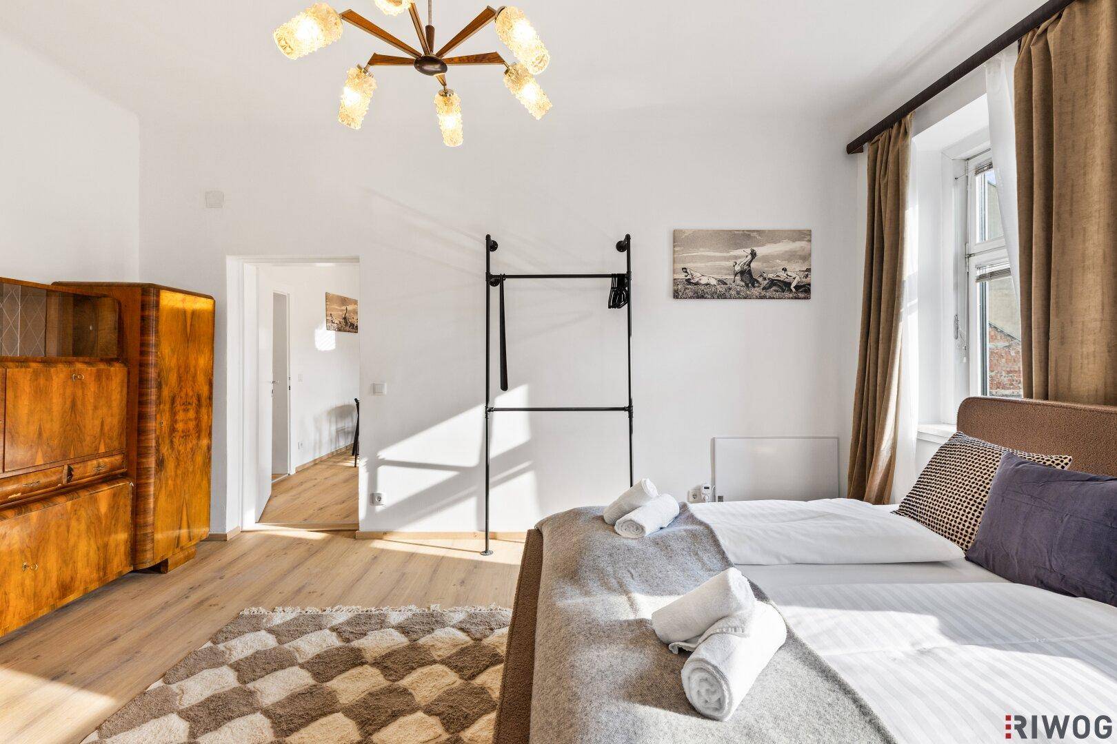 Schlafzimmer mit Holzboden, Kleiderständer und Zugang zu weiteren Räumen.