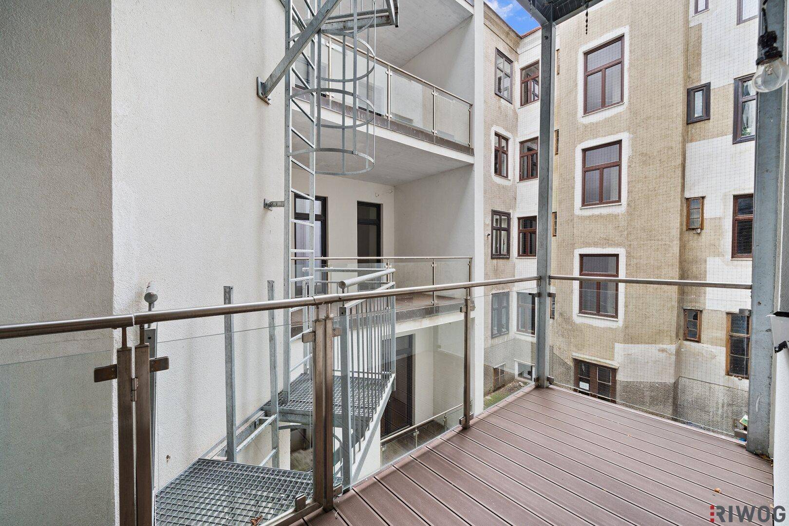 Moderner Balkon mit Holzbelag, Glasgeländer und einer Wendeltreppe zu weiteren Ebenen.