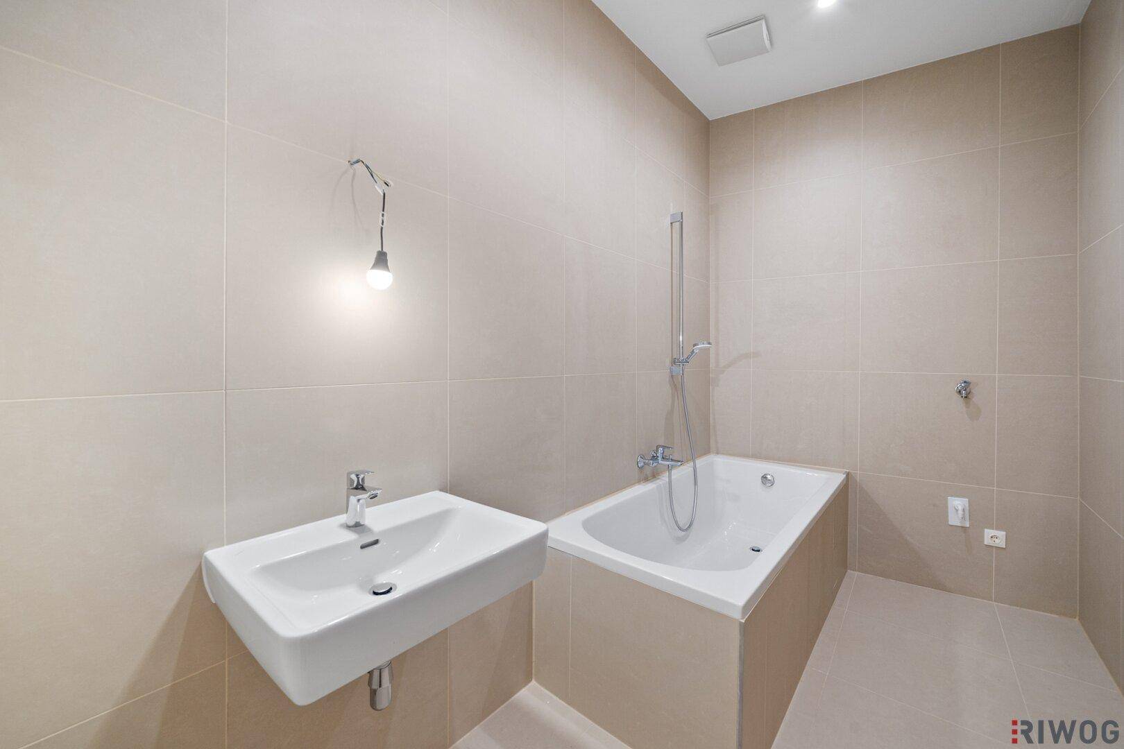 Modernes Badezimmer mit beigefarbenen Fliesen, Badewanne und Einzelwaschbecken.